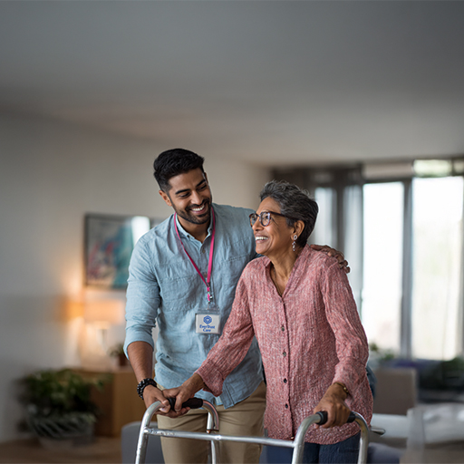Caregiver assisting happy elderly client using a walker.