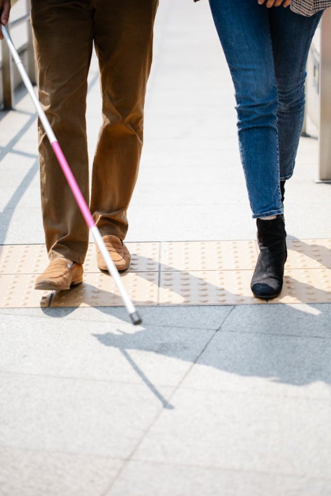 Two individuals walking side by side, one using a white cane for guidance.